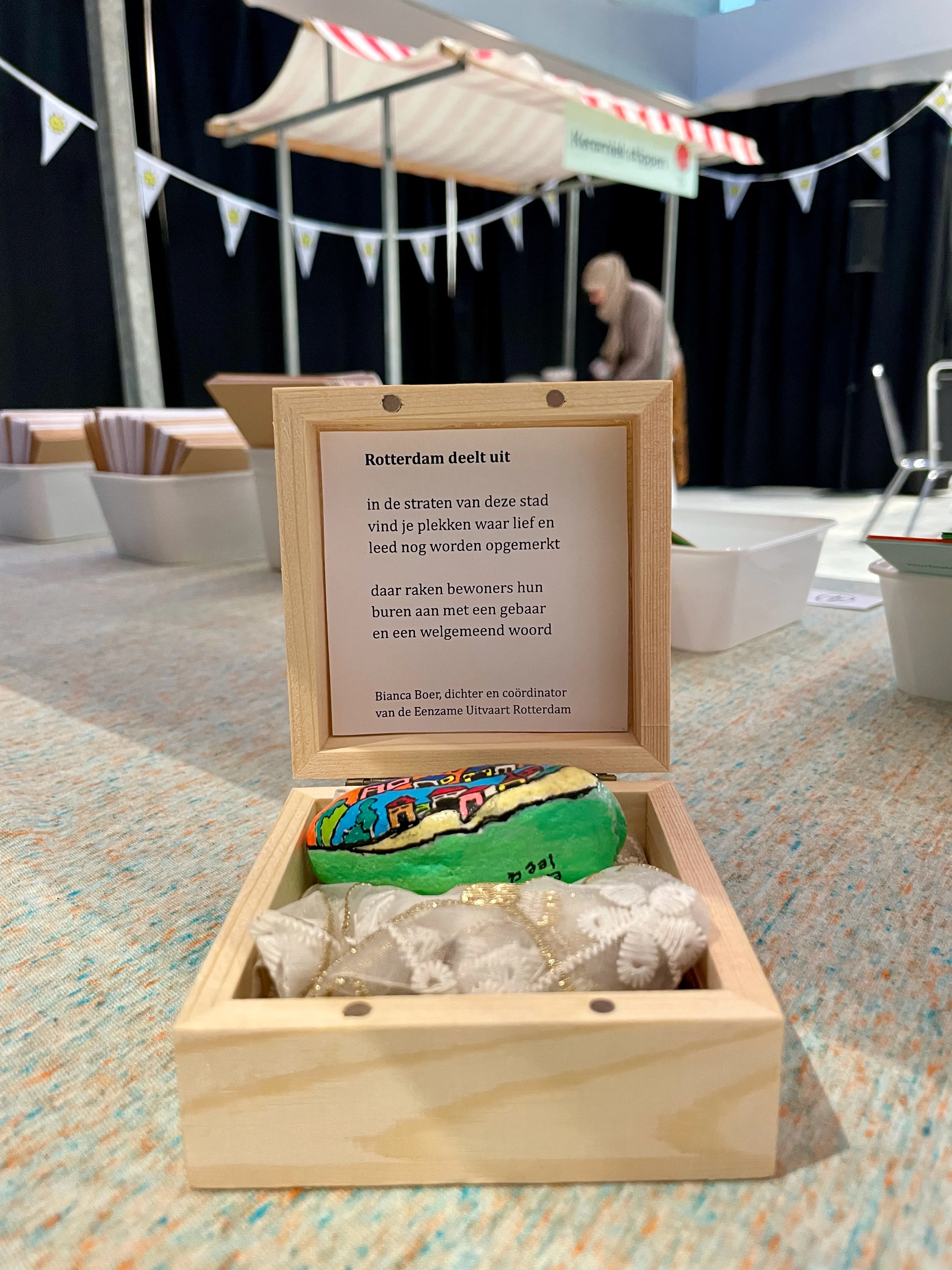 Foto van een marktkraam met op de voorgrond een houten doosje. In het deksel van het doosje zit een gedicht.